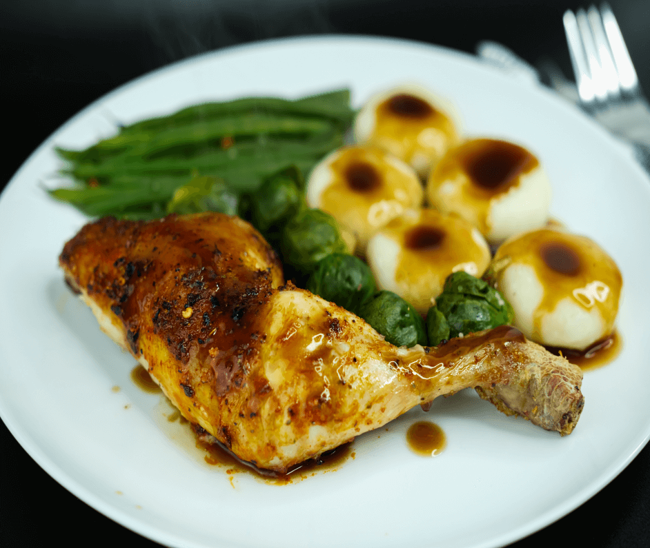 A white plate with a roast chicken leg and roast vegetables.